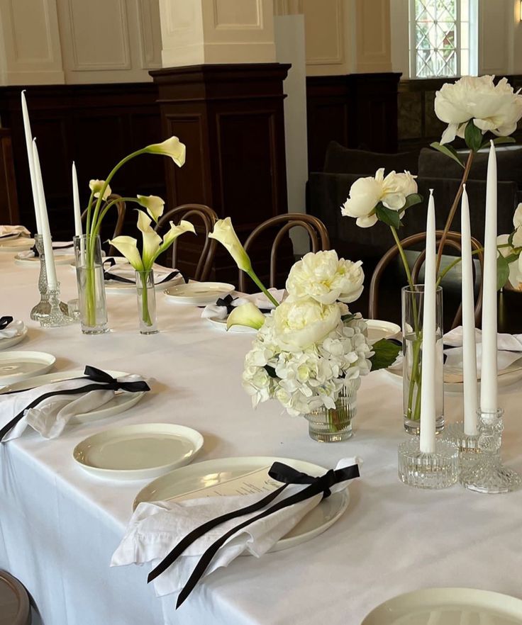 the table is set with white flowers and black ribbons on it, along with candles