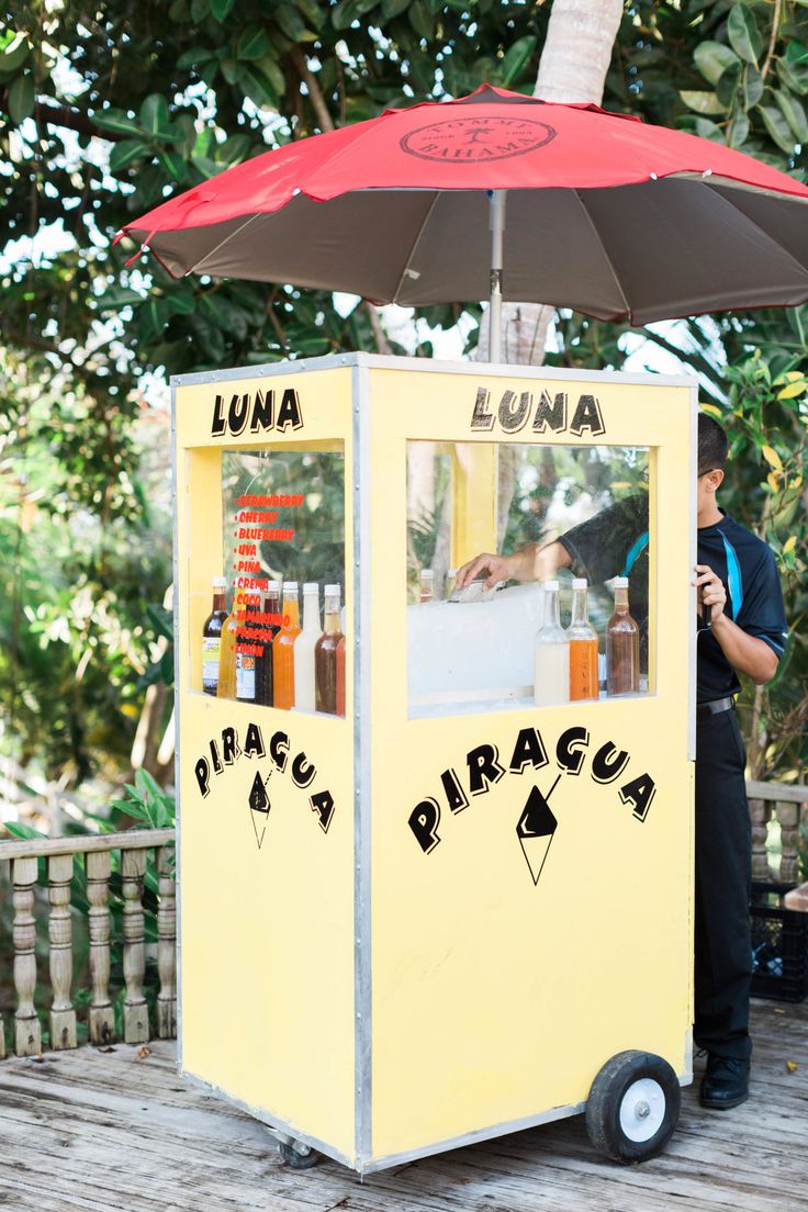 a man standing in front of a lemonade kiosk with an umbrella over it