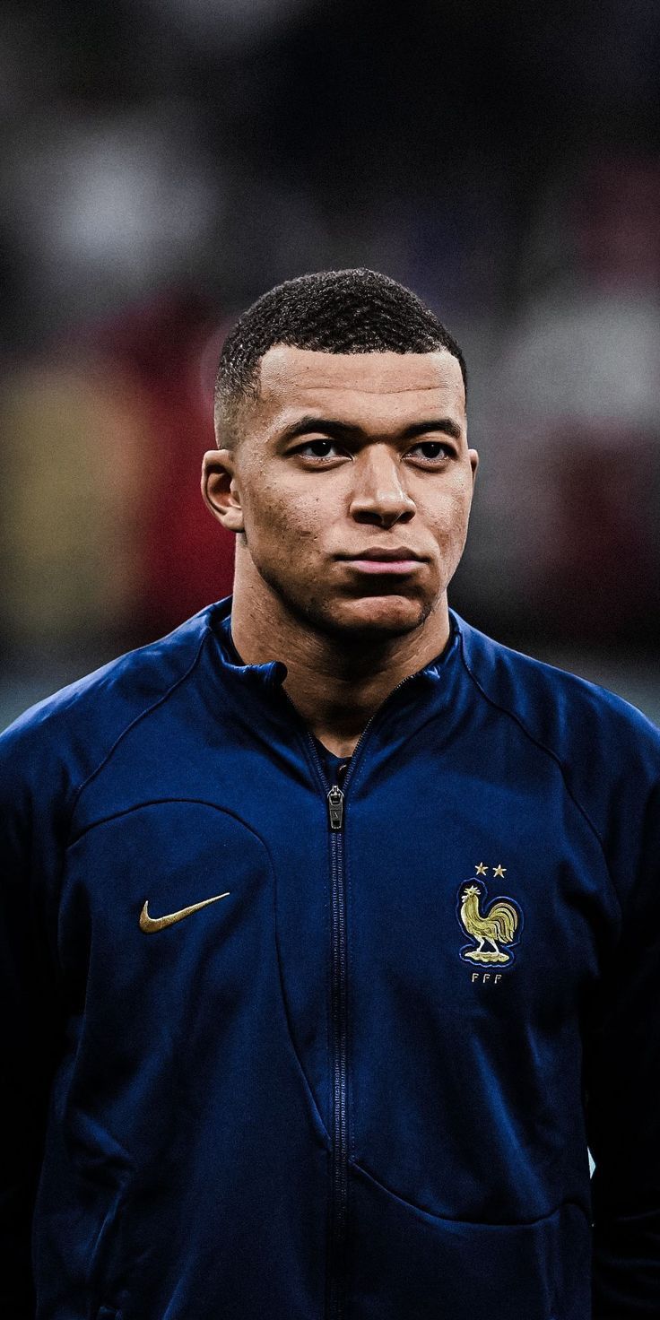 a close up of a soccer player wearing a blue jacket and looking at the camera