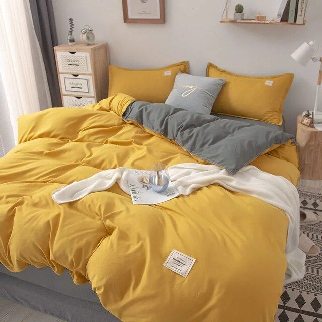 a bed with yellow sheets and pillows in a room next to a white wall,