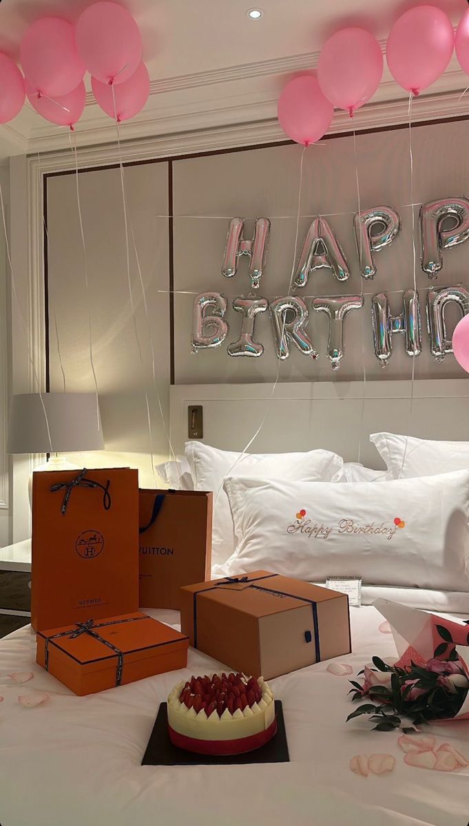 a birthday party with balloons, cake and boxes on the bed in front of it