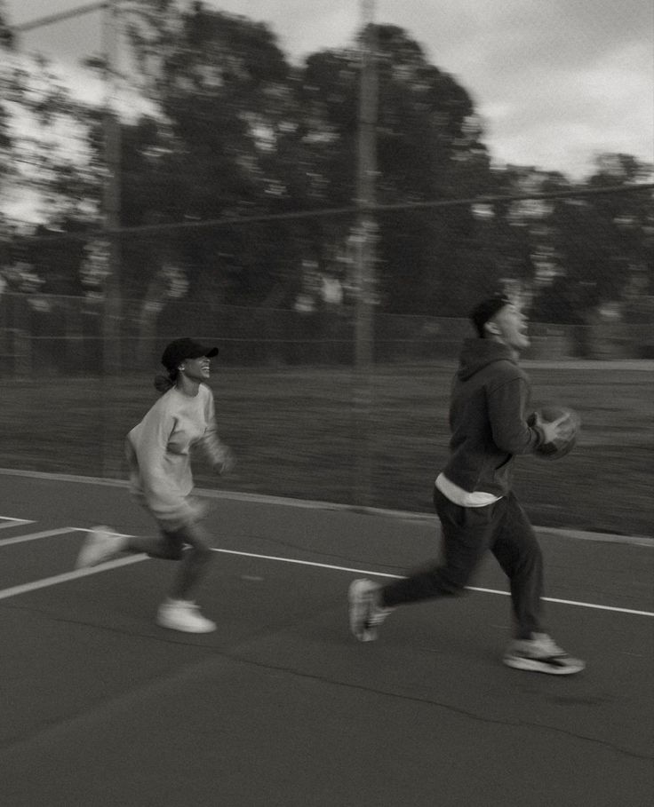 two people running on a tennis court with trees in the backgrouds behind them