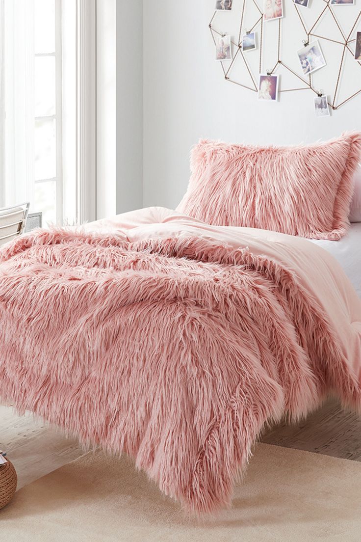 a bed with pink fur on it in a bedroom next to a white wall and window