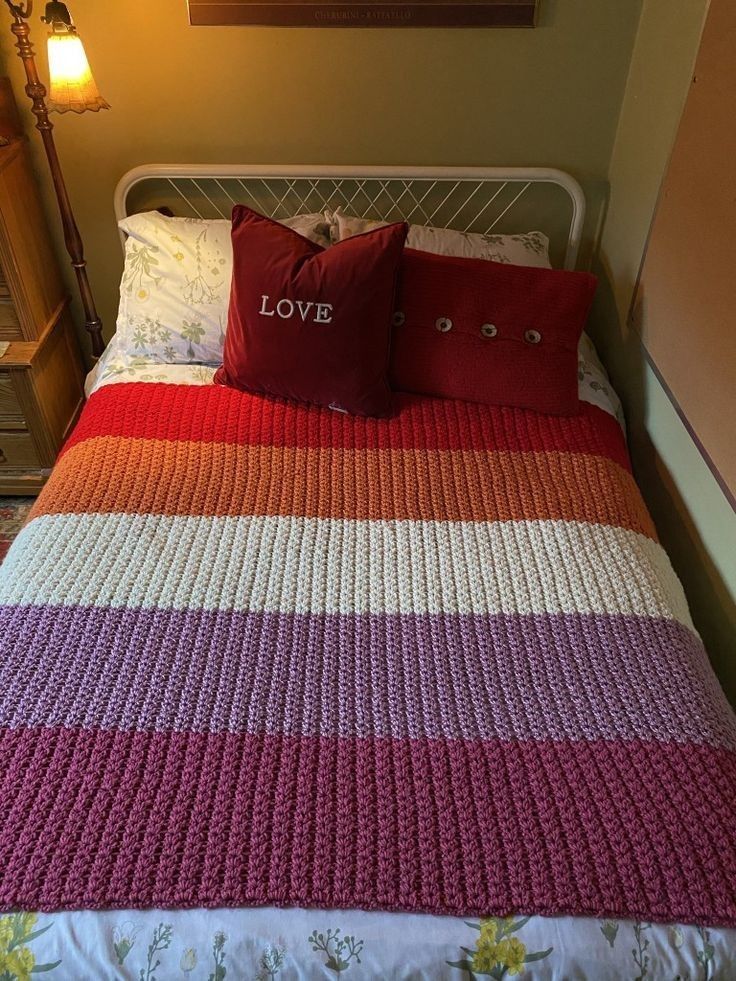 a bed with two pillows on top of it and a crocheted blanket in the middle