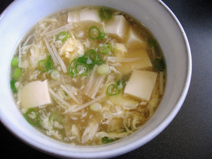 a bowl of soup with tofu, peas and cheese in it on a table