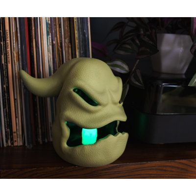 a green mask with glowing eyes and mouth is sitting on a shelf next to a record player