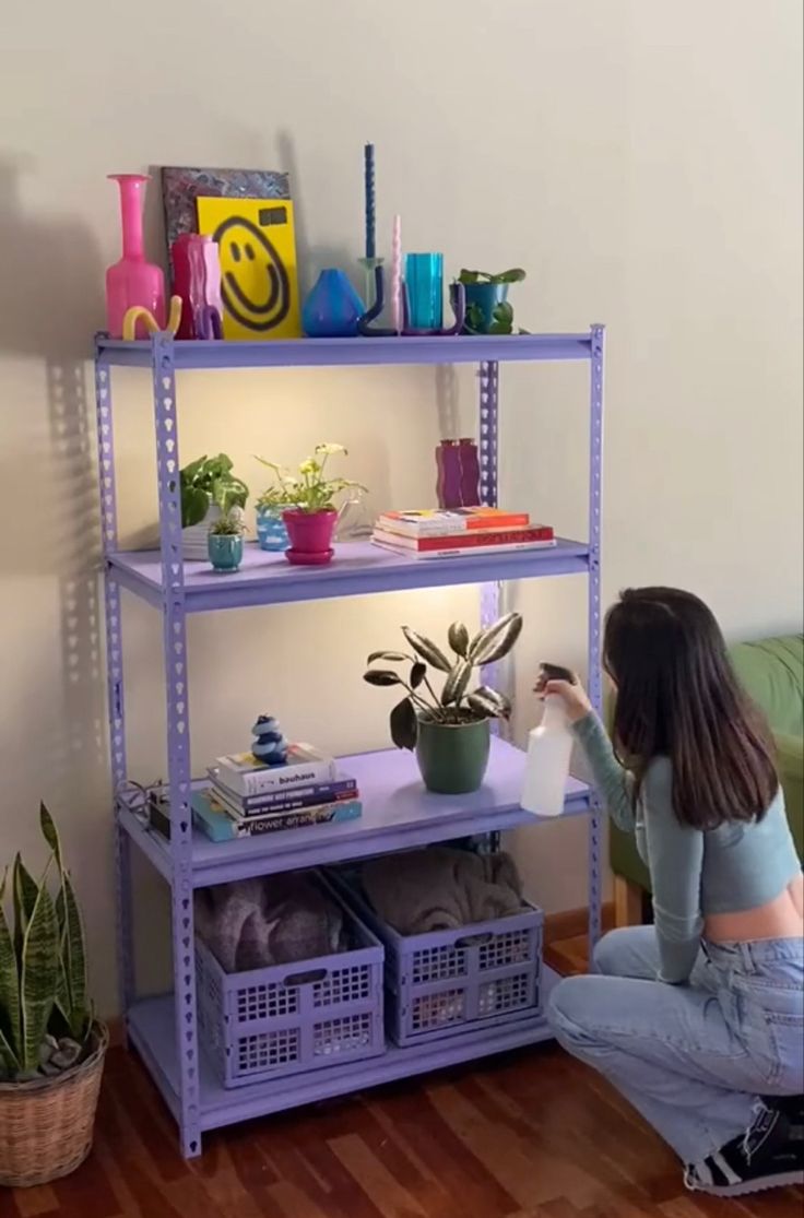 a woman kneeling down in front of a shelf filled with plants and other things on top of it