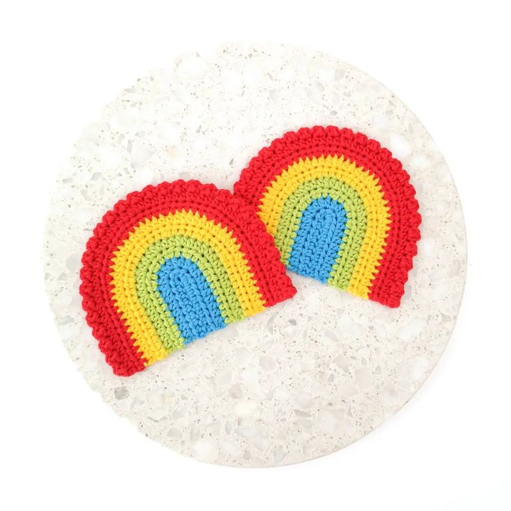 two crocheted rainbow coasters sitting on top of a white surface