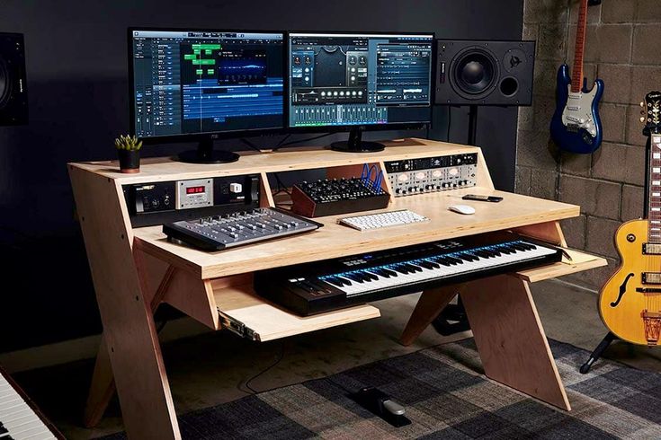 a desk with two monitors, keyboard and other electronic equipment on top of it in front of a guitar