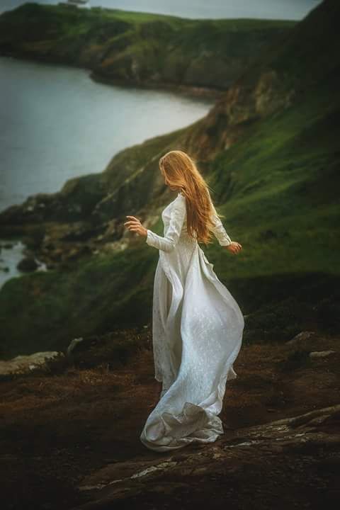 a woman standing on top of a lush green hillside next to a body of water