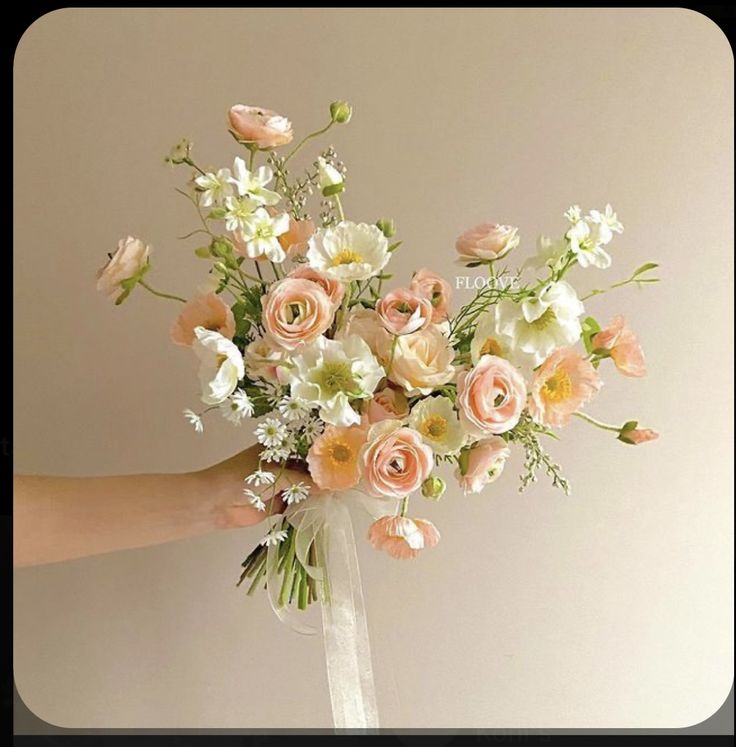 a person holding a bouquet of flowers in their hand with white and peach colors on it