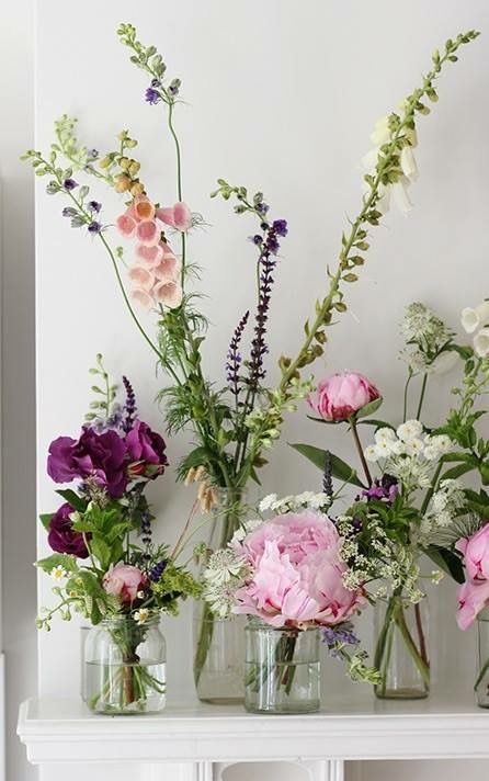 several vases with flowers in them sitting on a shelf next to a white wall