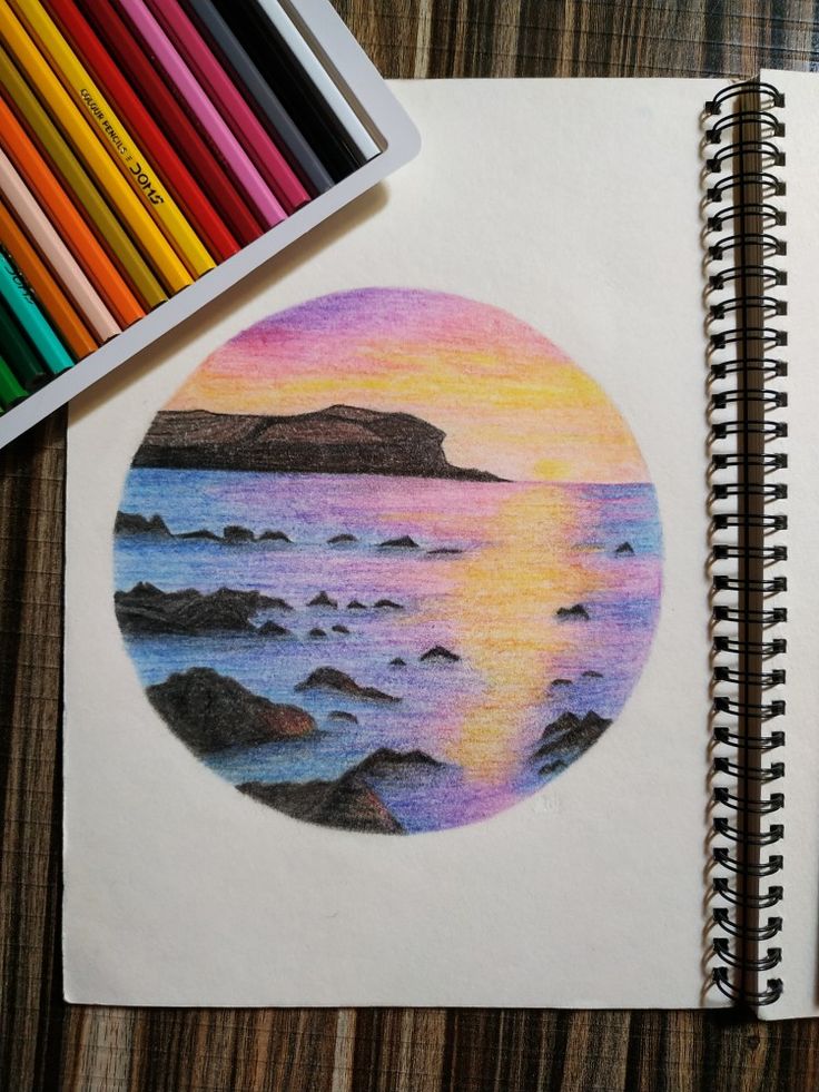 a drawing with colored pencils on top of it next to a notebook and crayons