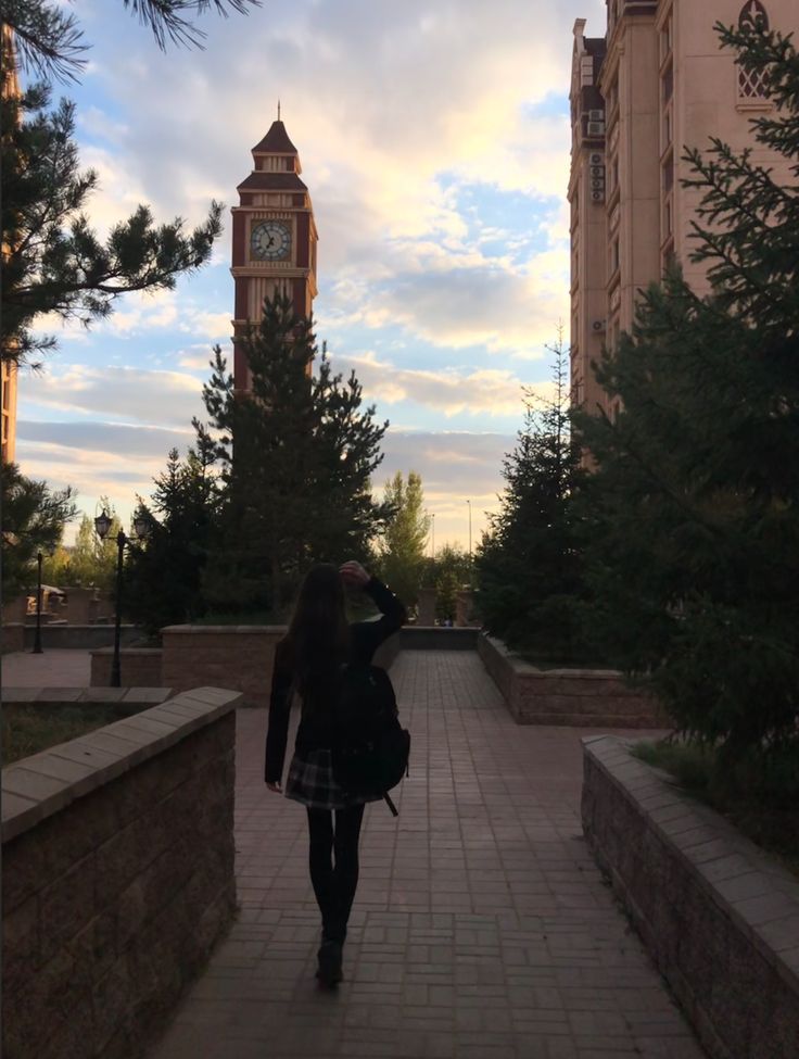 a woman walking down a sidewalk in front of a clock tower