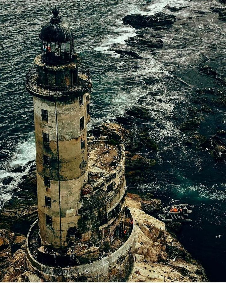 an old lighthouse sitting on top of a rocky cliff next to the ocean with waves crashing around it