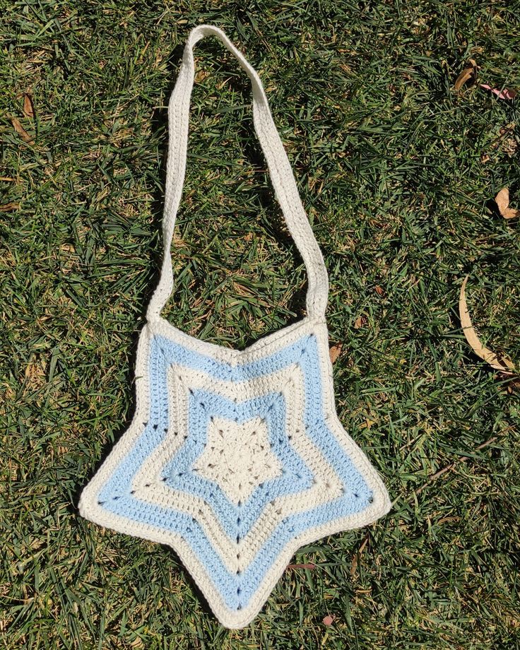 a crocheted blue and white bag laying on the grass with it's star shaped design