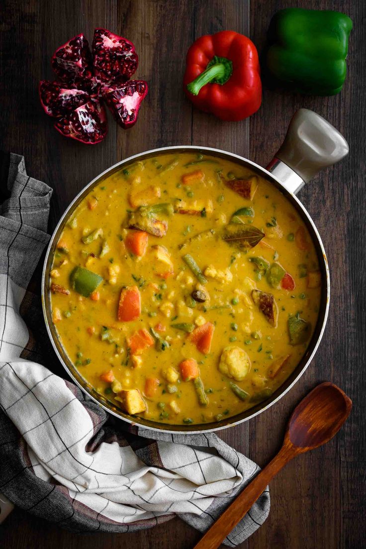 a pan filled with yellow curry next to peppers and other ingredients on a wooden table