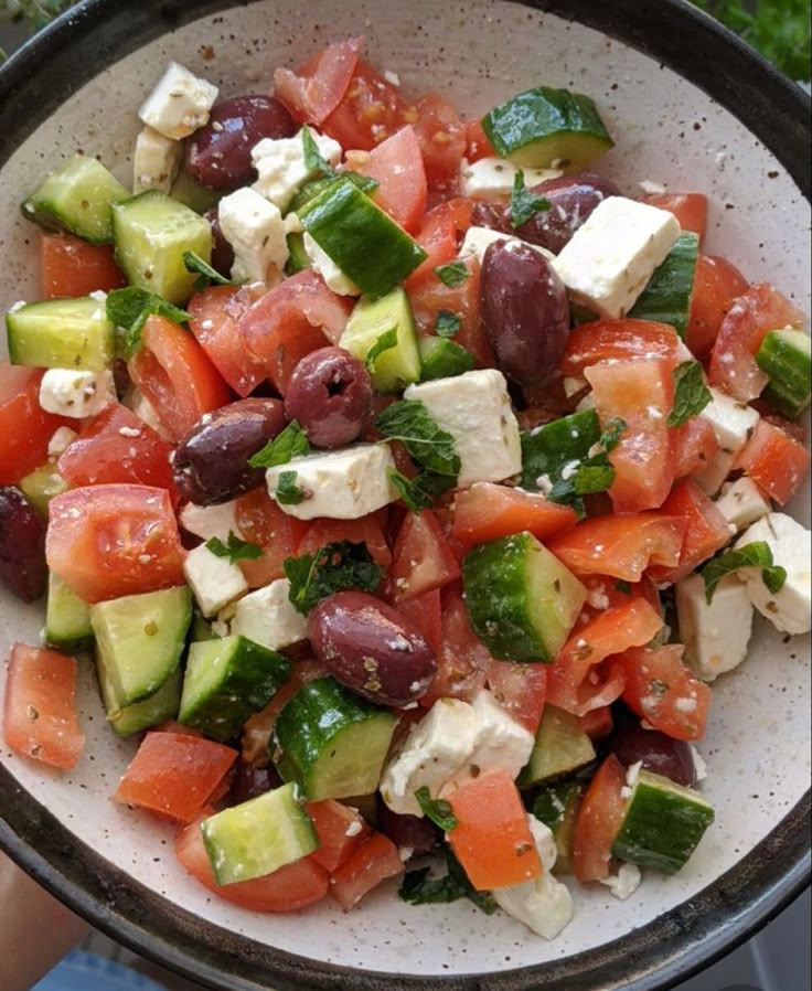 a bowl filled with cucumber, tomato and feta cheese on top of lettuce