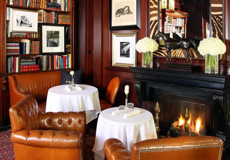 two leather chairs sitting next to each other in front of a fire place and bookshelf