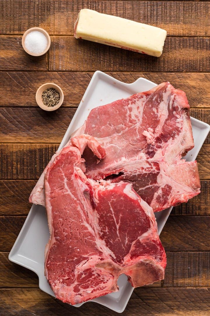 two pieces of raw meat sitting on top of a white plate next to some spices