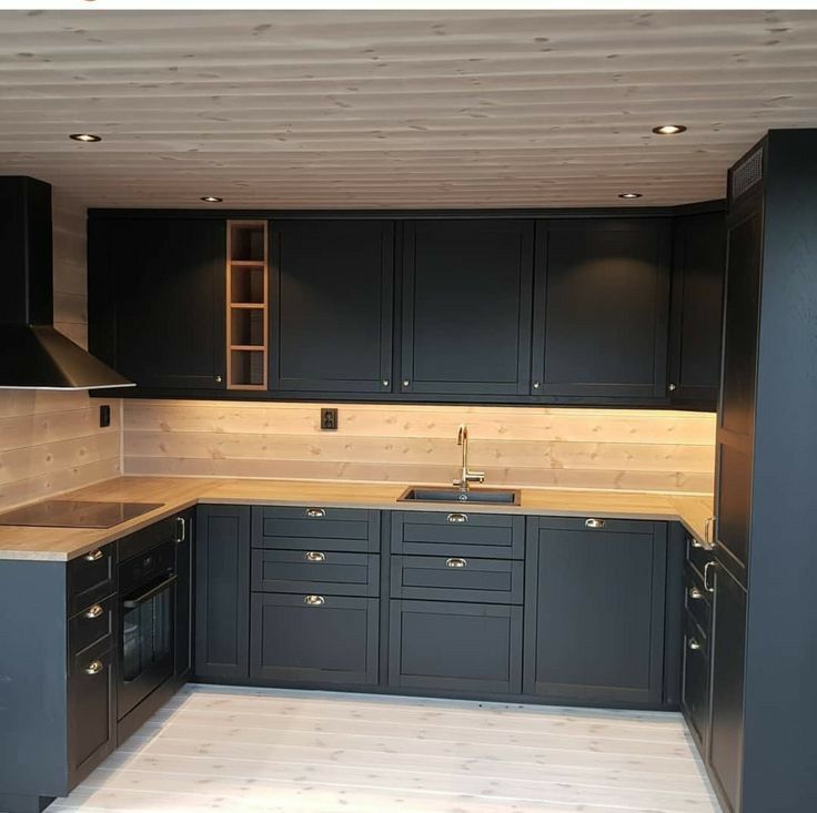 an empty kitchen with black cabinets and wood flooring on the walls is seen in this image