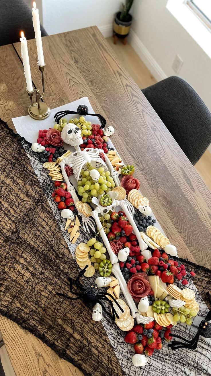 a table topped with a cake covered in fruit and skeleton figurines next to a lit candle