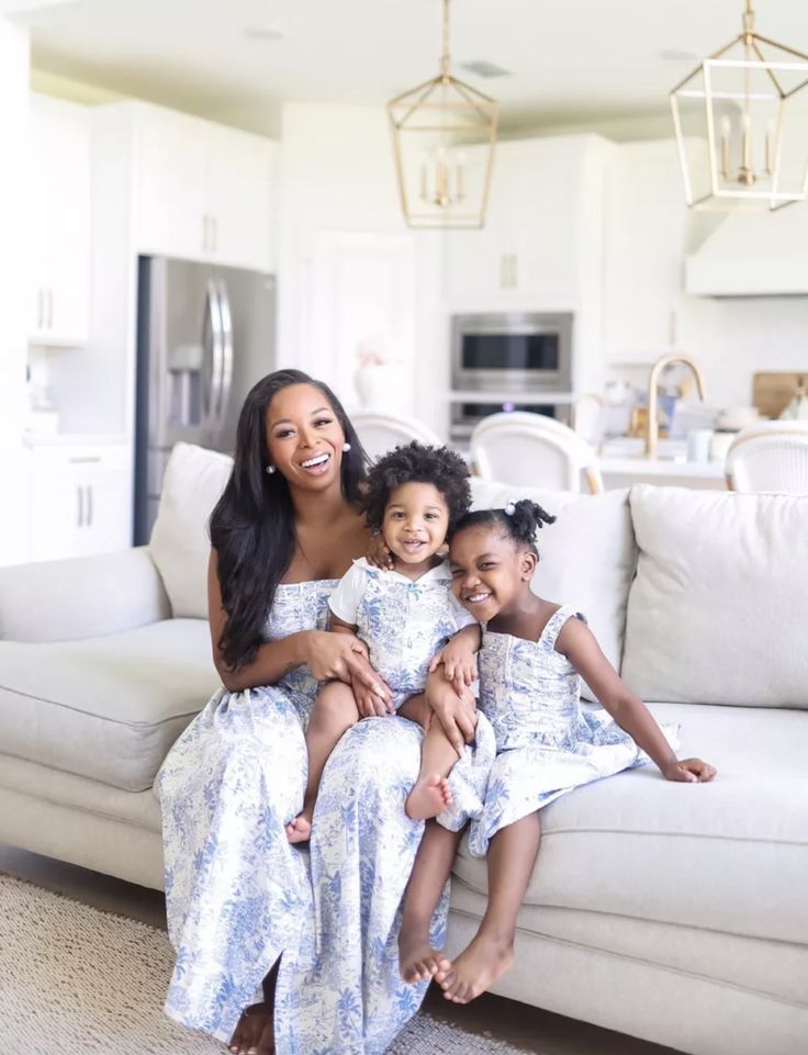 a woman and two children sitting on a couch in a living room with white furniture