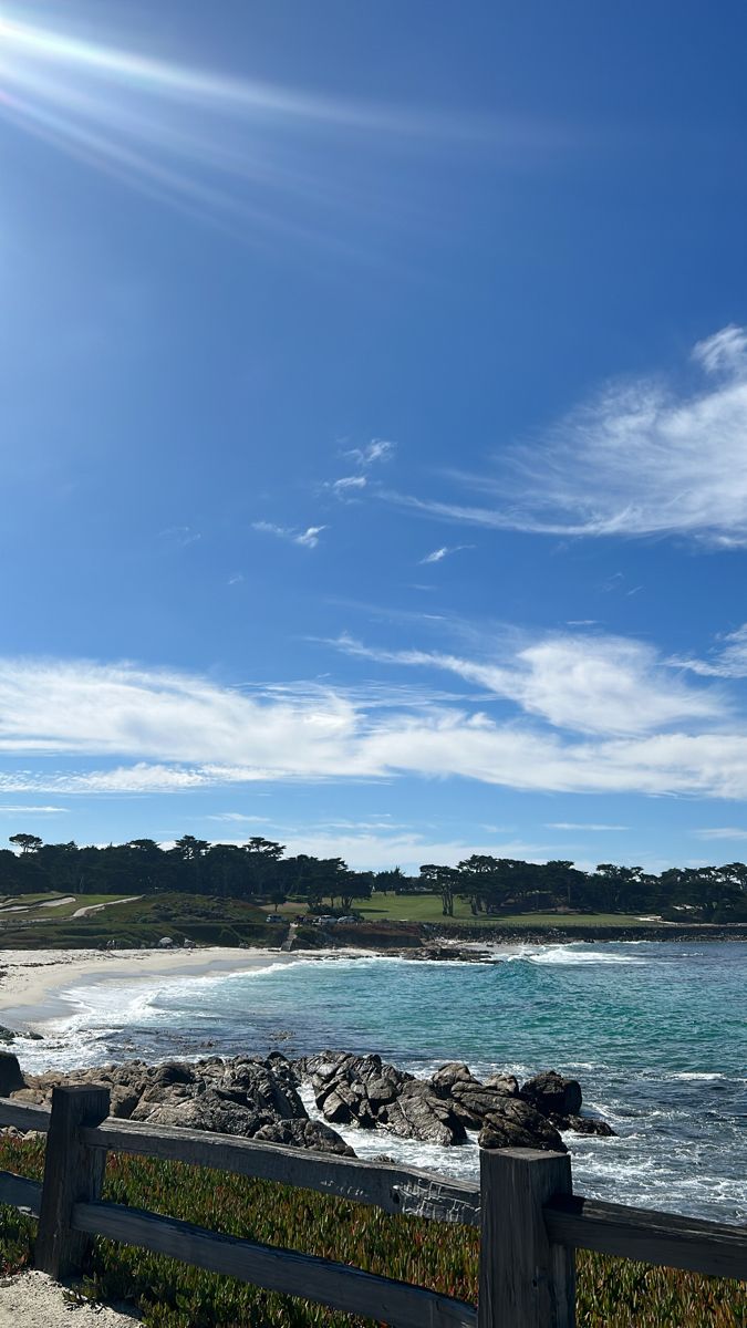 a wooden fence next to the ocean on a sunny day with clouds in the sky