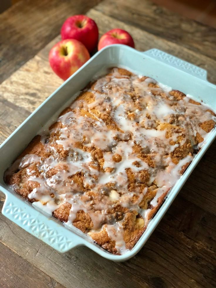 an apple dessert in a blue casserole dish with icing and apples on the side