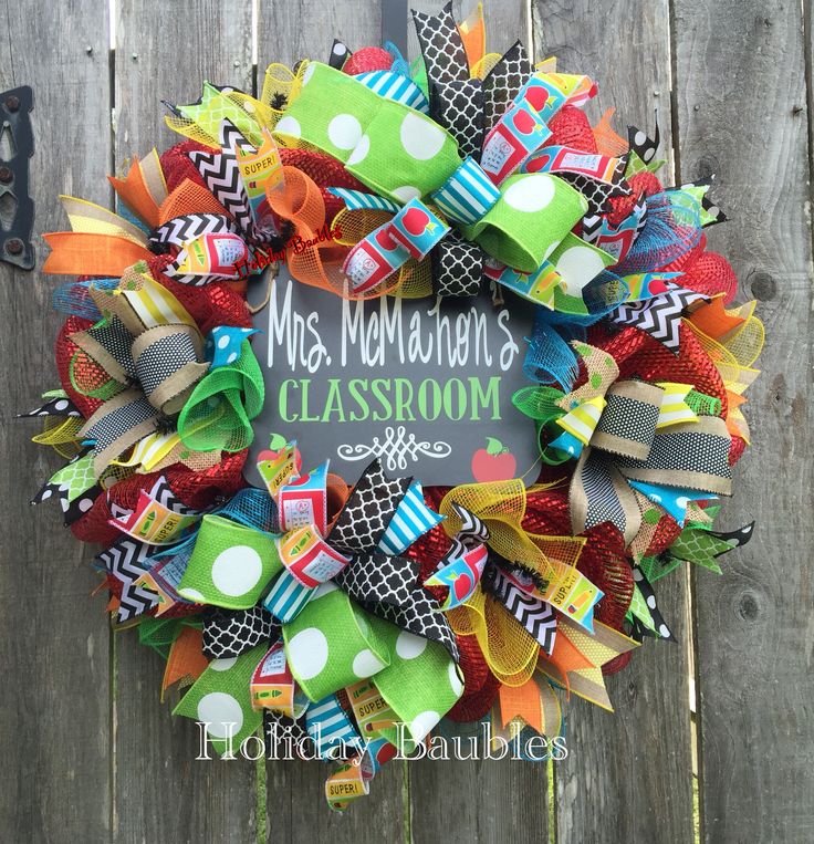 a colorful classroom wreath hanging on the side of a wooden fence that says mrs nomadson's classroom