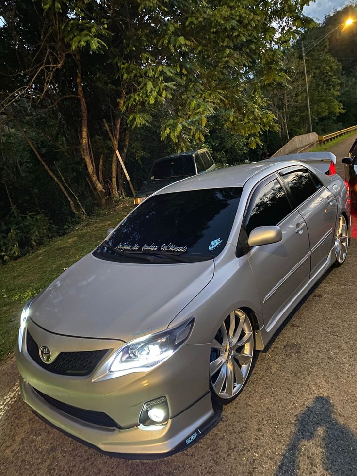 a silver car parked on the side of a road next to a person holding an umbrella