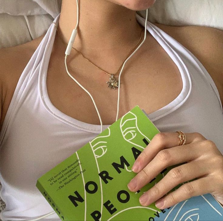 a woman laying in bed with headphones on her ears and holding a green book