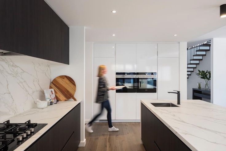 a woman walking through a kitchen next to a stove top oven and countertop covered in white marble