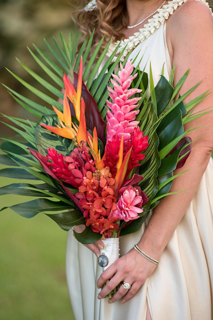 a woman in a white dress holding a bouquet of flowers and palm fronds