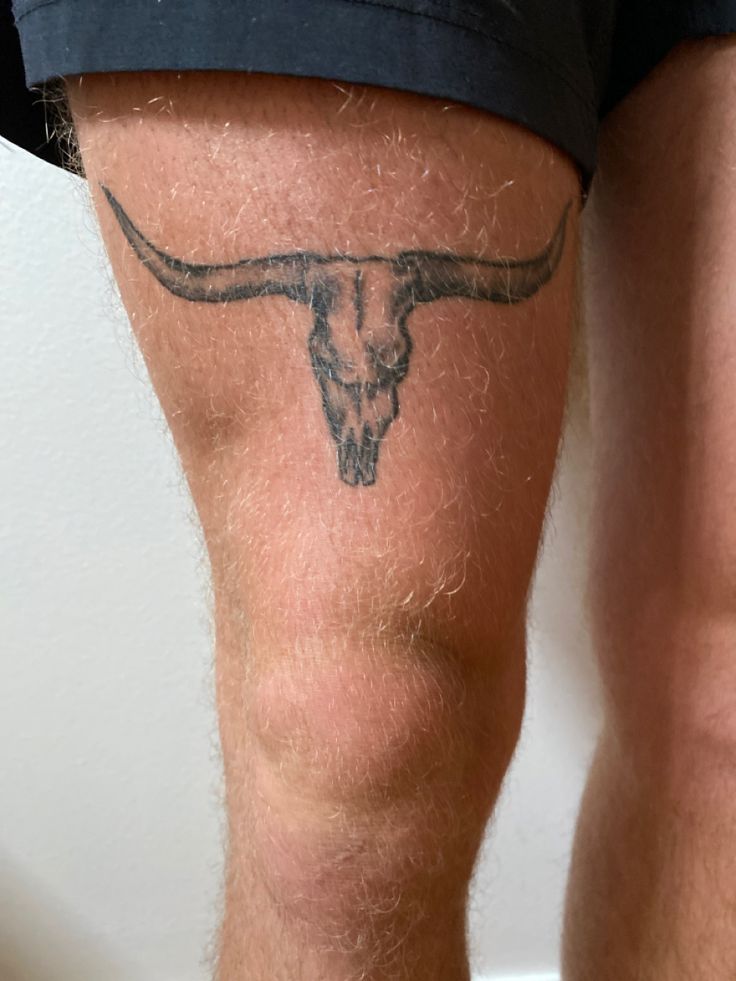 a close up of a man's legs with a bull skull tattoo on it