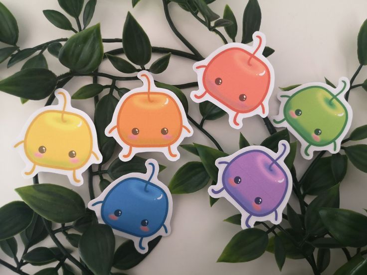 four colorful stickers with different shapes and sizes on them, sitting next to some leaves