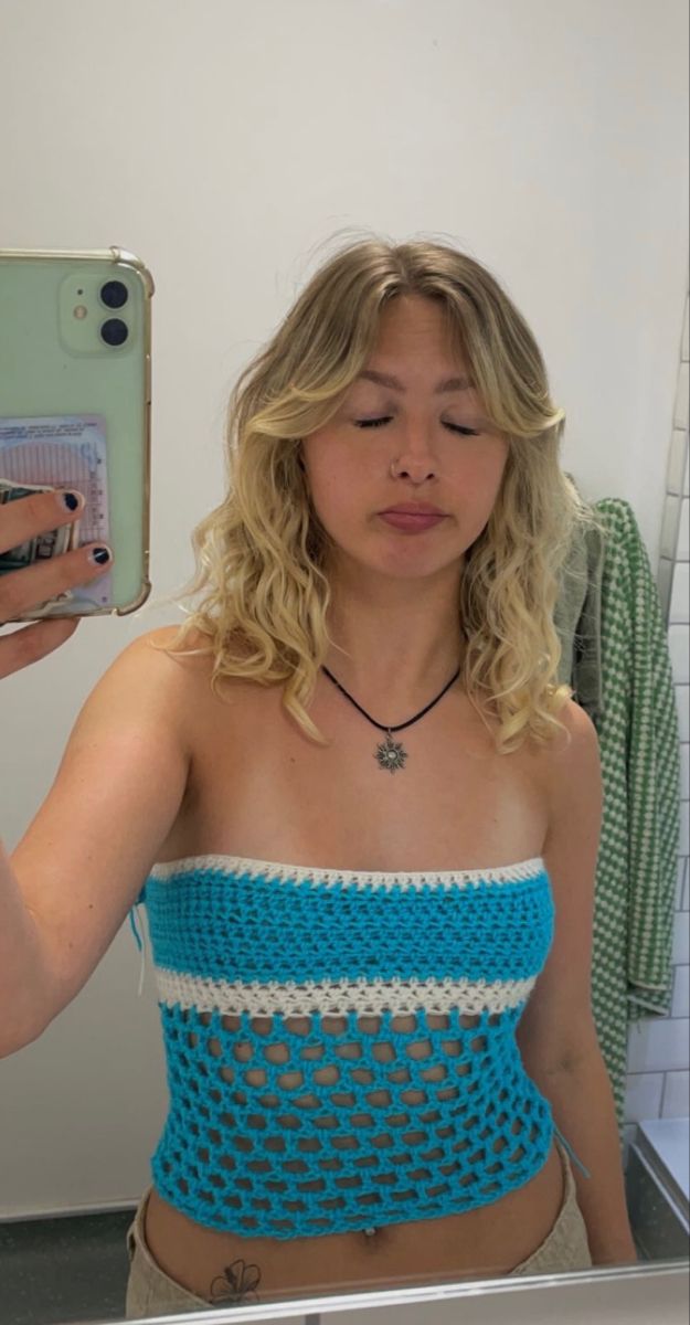 a woman taking a selfie in front of a mirror wearing a blue and white crocheted top