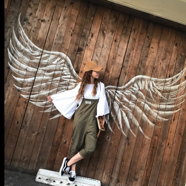 a woman standing in front of a wooden wall with wings painted on it