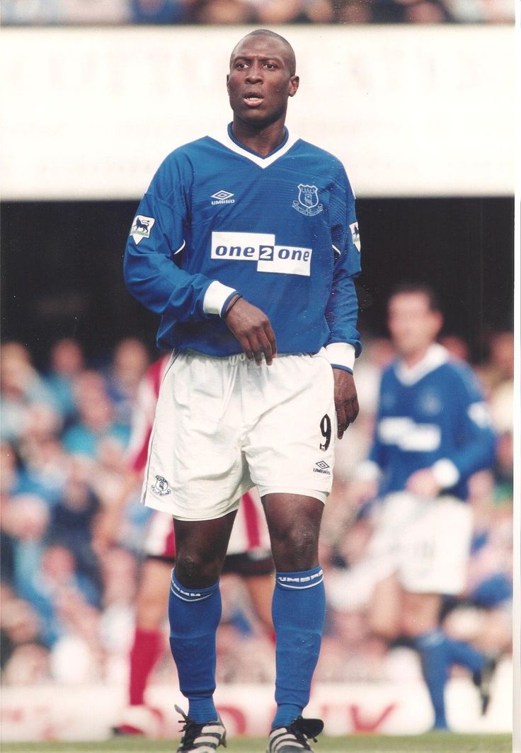 a man standing on top of a soccer field wearing blue and white uniform with his hands in his pockets