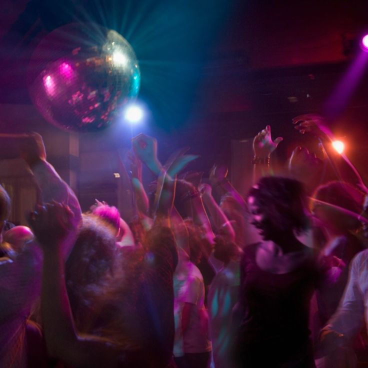 a group of people dancing at a party with disco balls in the air and lights on