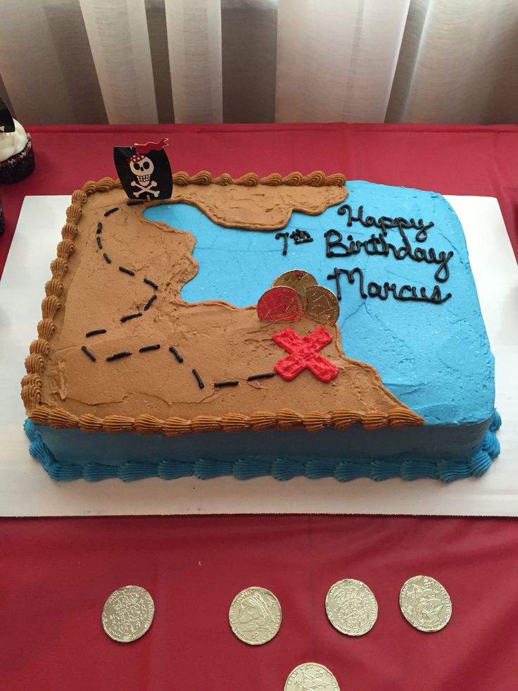 a birthday cake is decorated with a pirate map and coins on a table in front of a red tablecloth