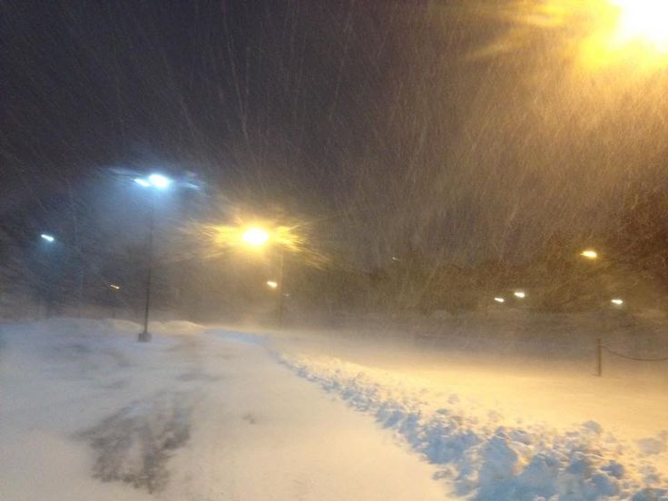 a snow covered street at night with light poles and street lamps in the background on a snowy day