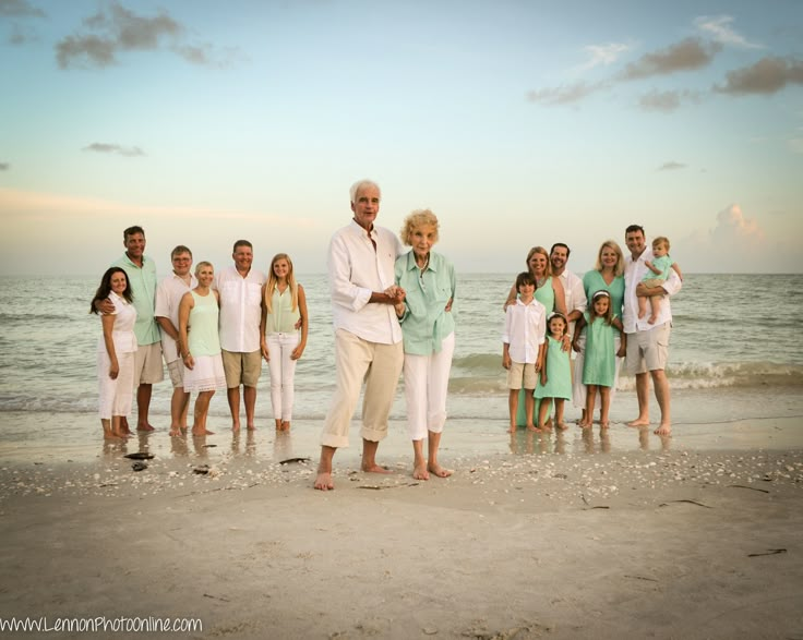 an older man standing in front of a group of people on the beach at sunset