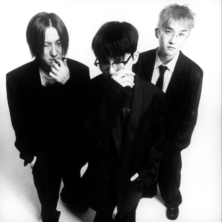 three young men standing next to each other in black suits and ties with their hands on their chins