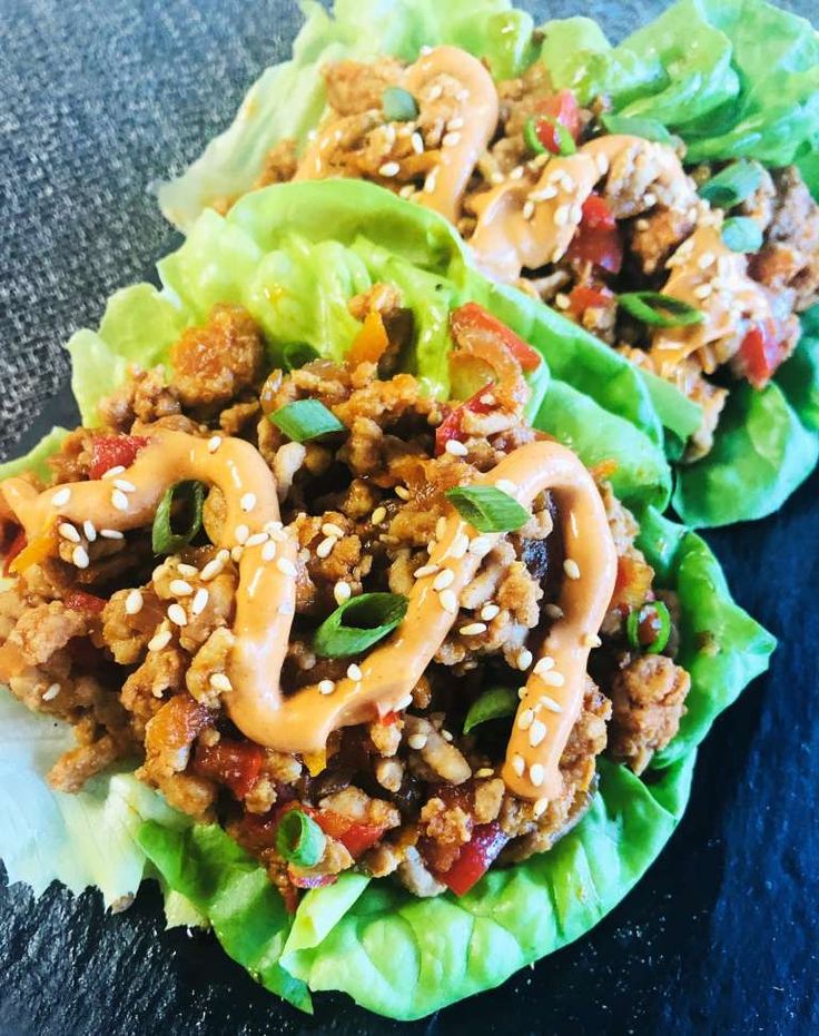 two lettuce wraps filled with meat and vegetables on top of a black surface