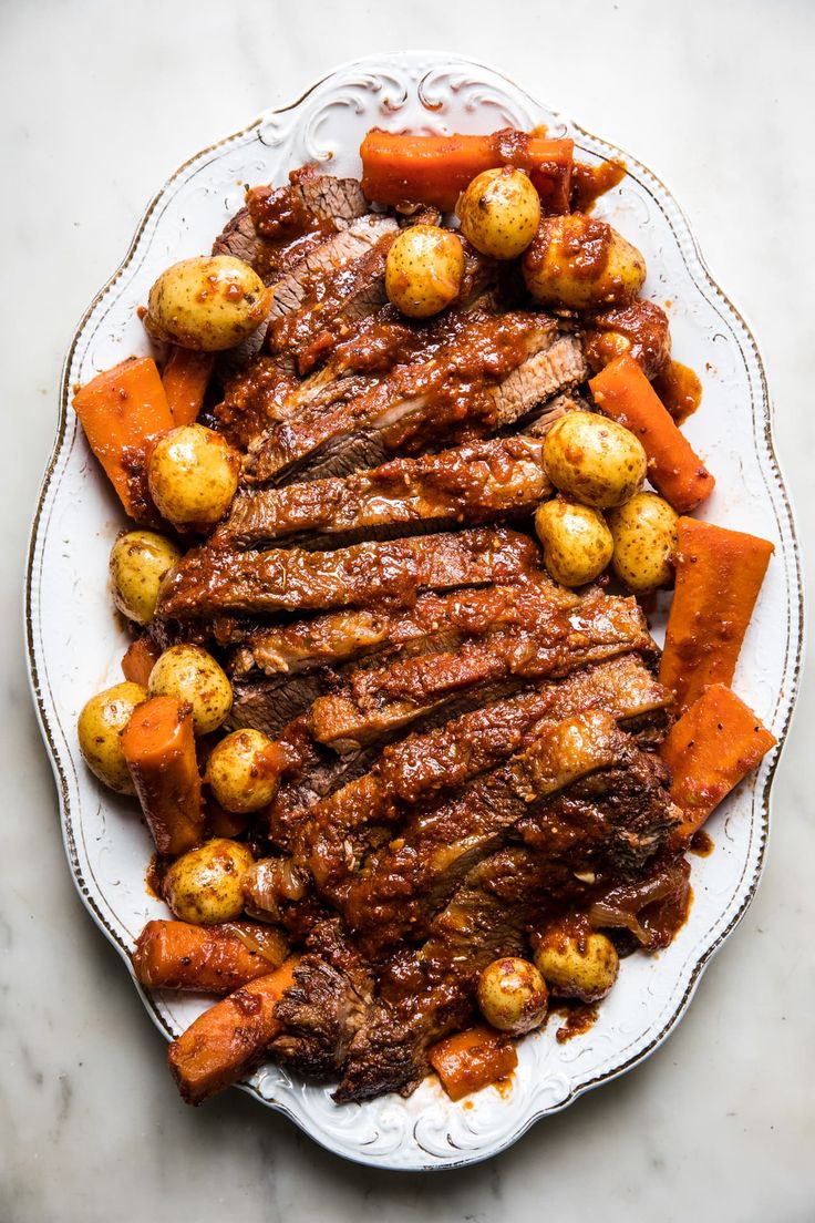 a plate with meat, potatoes and carrots sitting on a marble counter top next to a knife