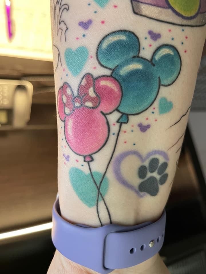 a person with a tattoo on their arm has a mickey mouse and minnie mouse balloon