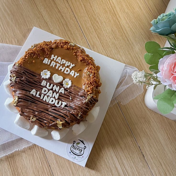 a birthday cake with chocolate frosting and flowers in the background on a card that says, happy birthday buna duna almonds