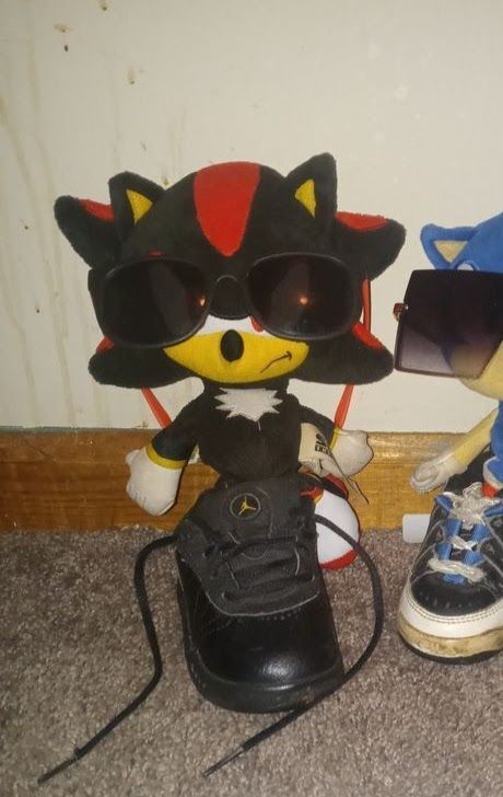 two stuffed animals with sunglasses and sneakers on the floor next to each other in front of a wall