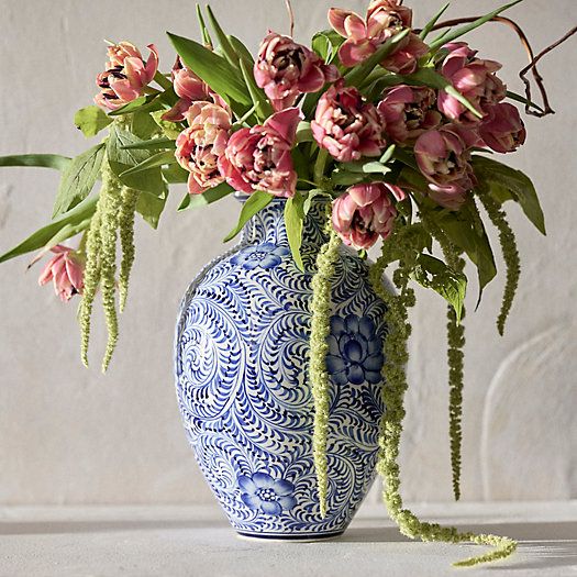 a blue and white vase filled with pink flowers on top of a table next to a wall